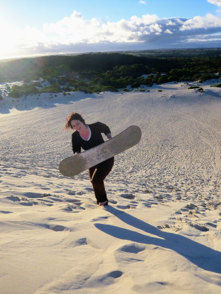 Maren Westphal trägt ein Sandboard eine Düne hinauf